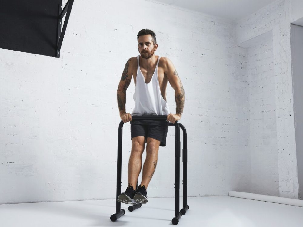 man performing weighted calisthenics on dip bar