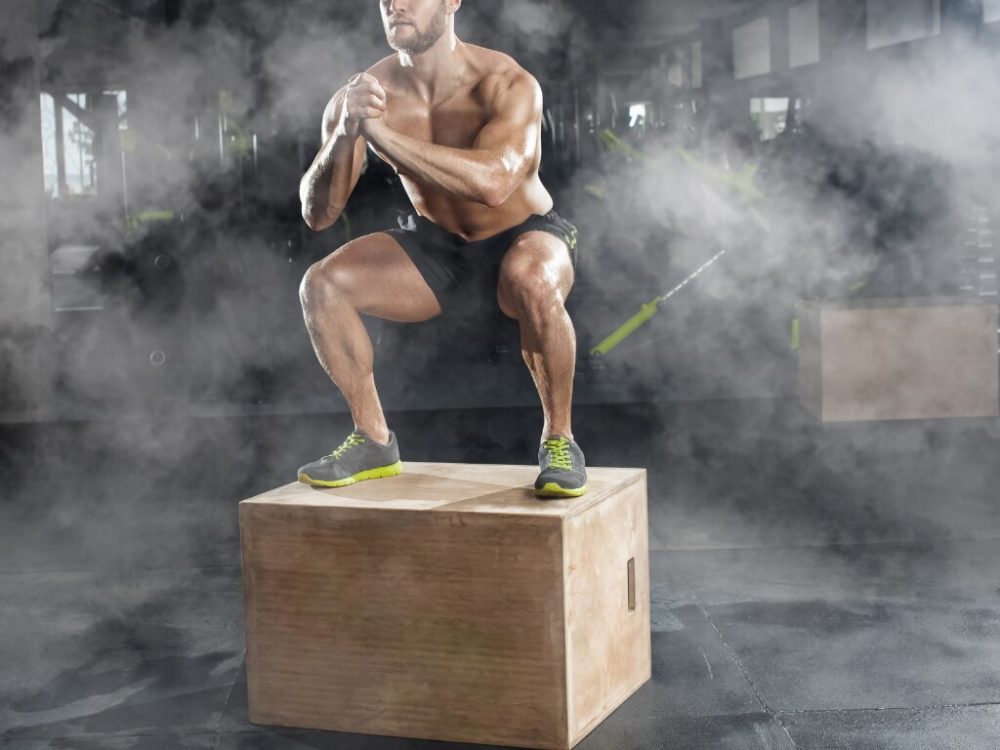 man squatting on a box showing off his muscles