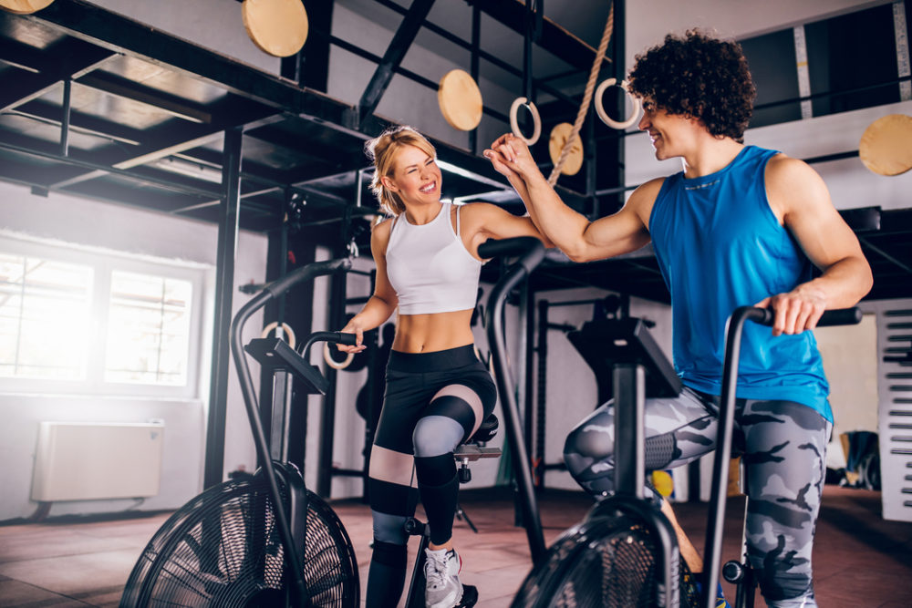Two people high fiving on air bikes